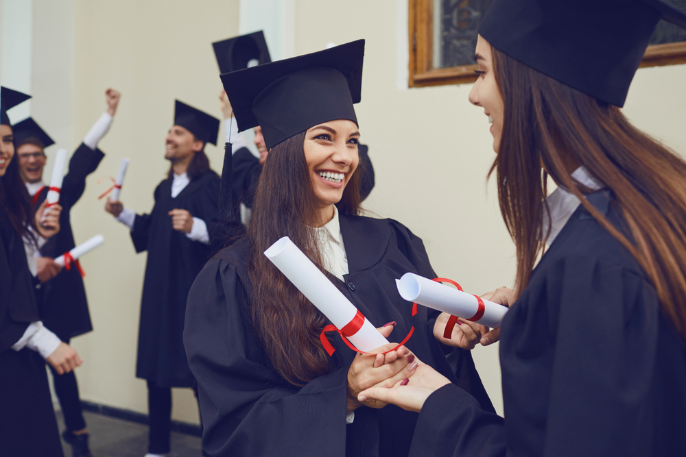 Shutterstock_1677330001 Female graduates with diplomas hugging laugh