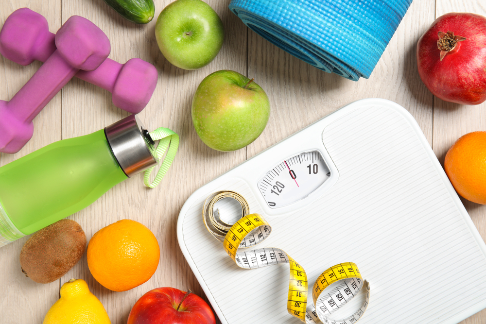 Shutterstock_1292487769 Flat lay composition with scales, healthy food and sport equipment on wooden background. Weight loss