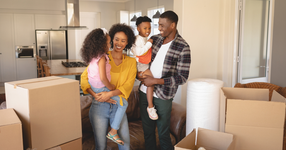 Shutterstock_1313986712 Front view of happy African American parents with their children and boxes moving in new house