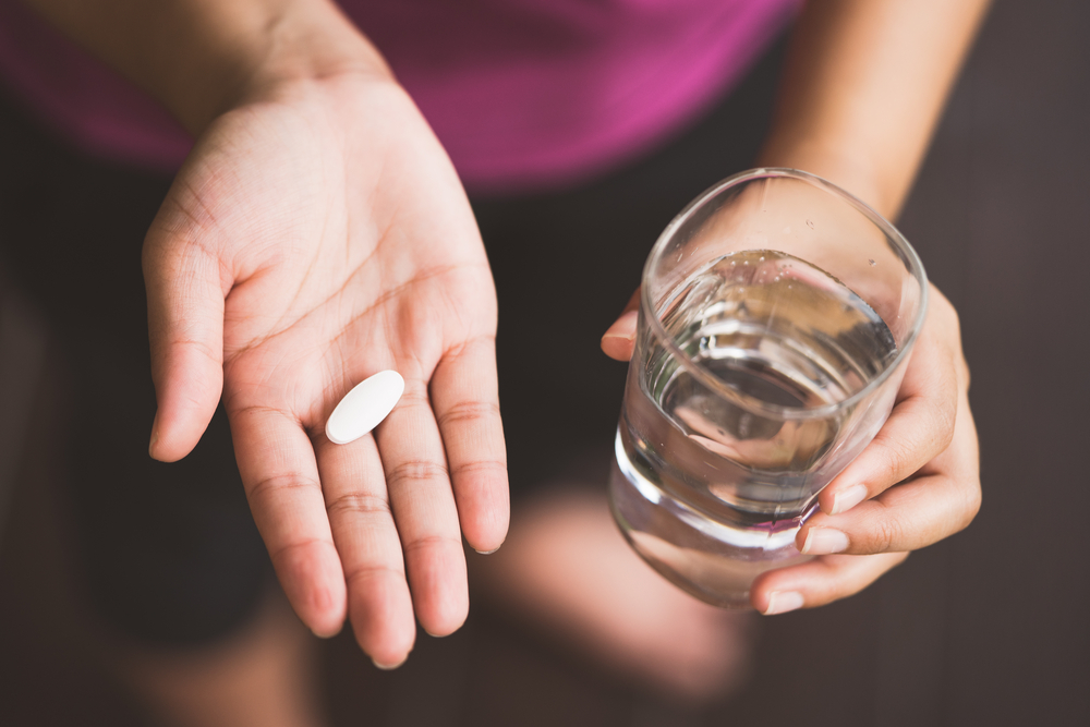 Shutterstock_718784776 Close Up Of Girl holding Pill and glass of water.With Paracetamol.Nutritional Supplements.Sport,Diet Concept.Capsules Vitamin And Dietary Supplements.