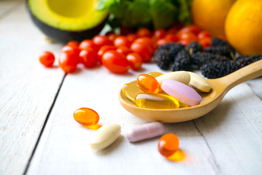 Shutterstock_1041373417 Pills and capsules in wooden spoon with fresh fruits. Multivitamins and supplement from fruits concept.