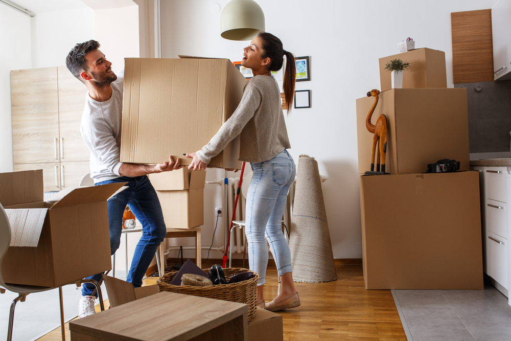 Shutterstock_568241401 Young couple carrying big cardboard box at new home.Moving house.